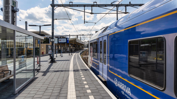 Trein van Arriva staat in bocht aan perron van station Venlo, je ziet het stationsgebouw in de achtergrond.
