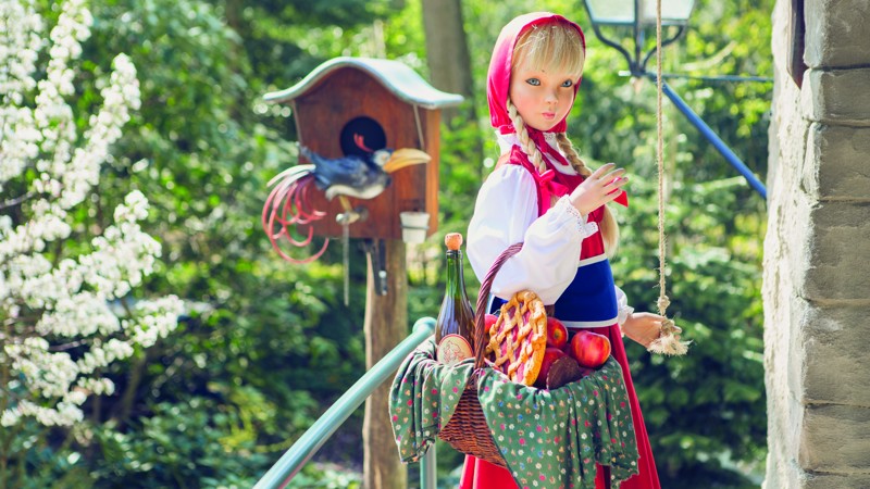 Een pop van roodkapje staat in het Sprookjesbos van de Efteling met een mandje vol eten voor een huisje.