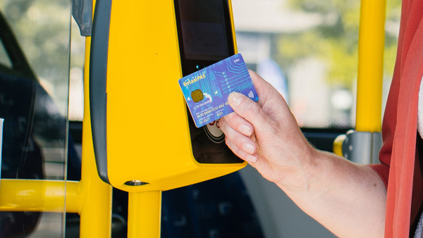 Iemand houdt een betaalpas voor een gele incheckpaal in een bus van Arriva.