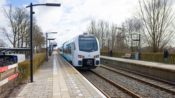 Blauwe trein van Arriva richting Leeuwarden staat stil op een klein station bij een leeg perron op een winterse dag.