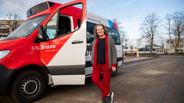 Lachende vrouw staat naast open deur van rood-wit buurtbusje in Brabant.