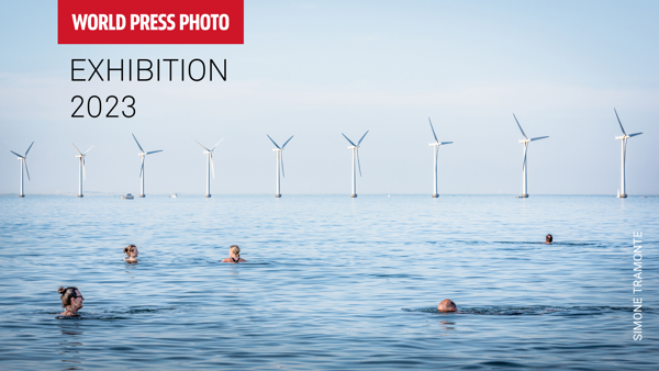 Advertentie voor World Press Photo 2023. Mensen die in een meer zwemmen met op de achtergrond windmolens.