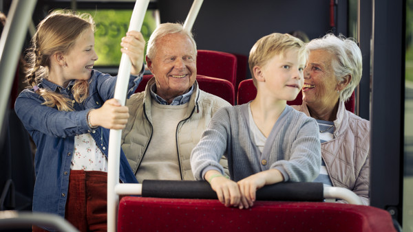 Een opa en oma zitten met hun kleinkinderen in een Arriva-bus. Ze lachen naar elkaar.