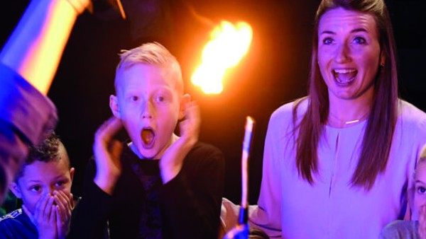 Een meisje en jongen worden felpaars verlicht terwijl ze geschrokken en verrast naar een hand met aansteker kijken.